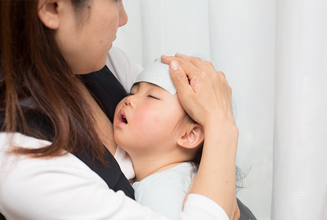 おでこを冷やす子供を抱っこする母親