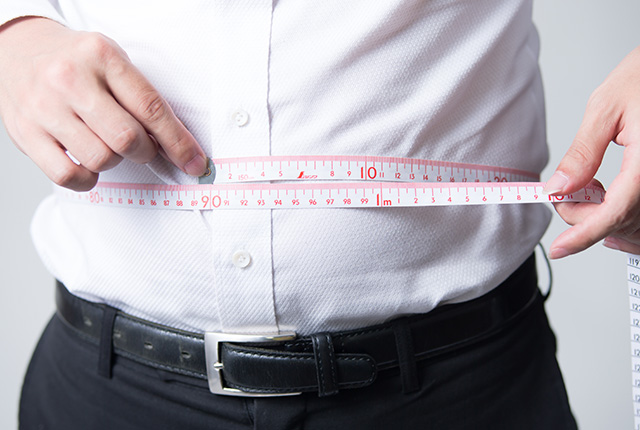 大きなお腹をした中年男性が服の上から腹囲を計測する様子
